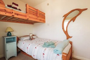 Ein Schlafzimmer mit einem Etagenbett, einem Nachttisch mit Lampe, einem Bett mit gemustertem Überwurf und einem Wandspiegel.