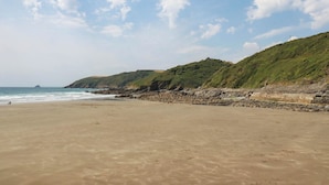 A beach with a rocky shoreline and a grassy hill in the background. - The Granary (Truro)