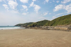 Ein Strand mit felsigem Ufer und einer grasbewachsenen Hügelkette im Hintergrund.