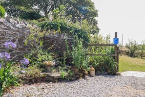 A stone wall with a wooden gate, surrounded by gravel and various plants. - The Granary (Truro)