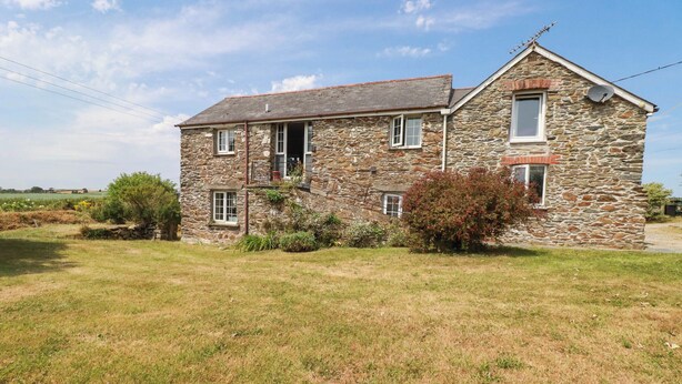 A two-story stone house with a sloped roof, a satellite dish, and a small garden area. - The Granary (Truro)