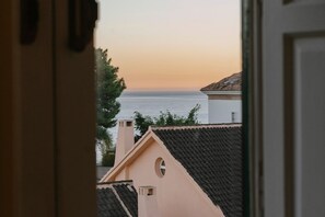 Une vue à travers une porte ouverte, donnant sur un bâtiment doté d’un toit en tuiles, d’une petite fenêtre et offrant un aperçu de la mer.