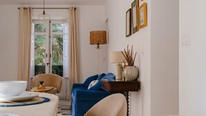 A room with a dining table set for two, a blue sofa, a lamp, and a view through a door. - Hacienda Clavero Seven Deluxe Apartment: (Málaga)