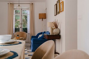 Ett rum med ett matbord dukat för två personer, en blå soffa, en lampa och en utsikt genom en dörr.