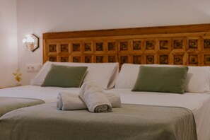 Ein Hotelzimmer mit hölzernem Kopfteil, zwei Betten mit grün-weißer Bettwäsche und einem zusammengerollten Handtuch auf dem Bett.