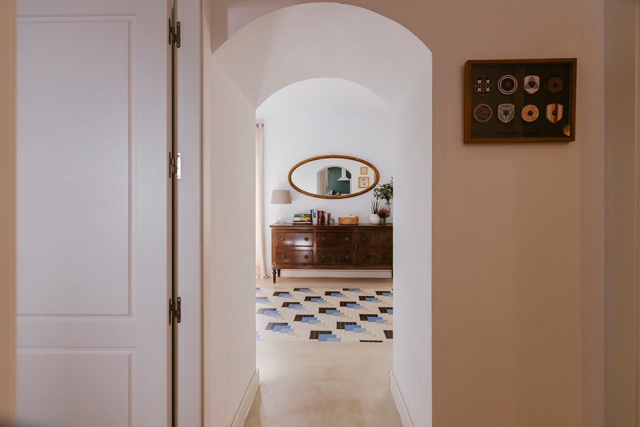 A hallway with a white door, a wooden cabinet, a mirror, and a framed collection of plates on the wall.