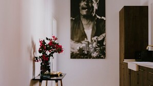Ett rum med en vit vägg, ett svartvitt fotografi, ett litet bord med en vas med röda blommor och ett träskåp med ett handfat.