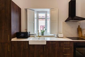 A kitchen with dark wood cabinets, a white sink, a black microwave, and a black range hood. - Hacienda Clavero Eight Ocean View Apartment (Málaga)