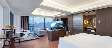 Habitación de hotel moderna con una cama grande, una mesa de comedor, un sofá, un televisor y vistas a la ciudad.