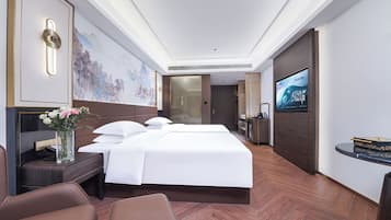 A hotel room with a large bed, a desk with a computer, a TV, and a wall-mounted artwork.