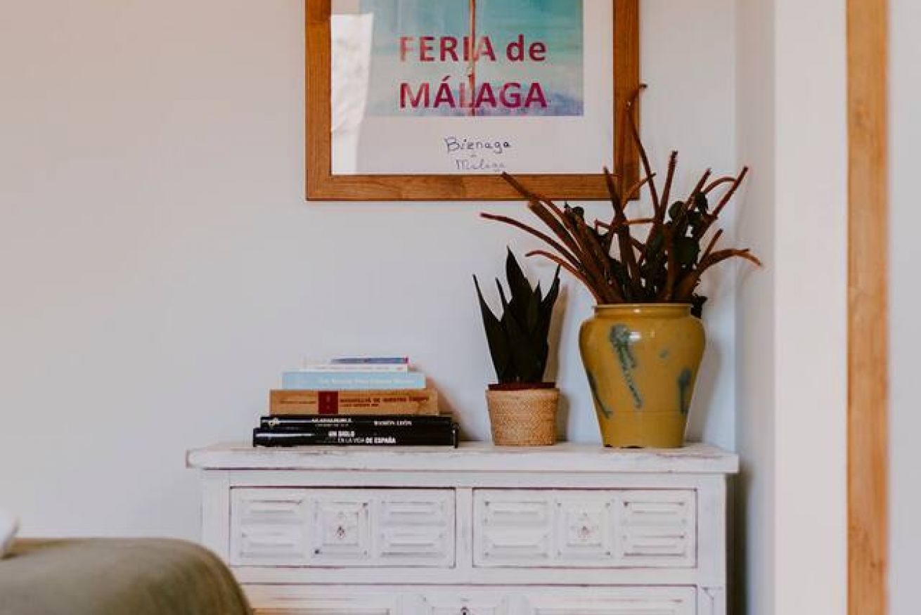 Un aparador blanco con un cuadro enmarcado, una planta en maceta y una pila de libros.