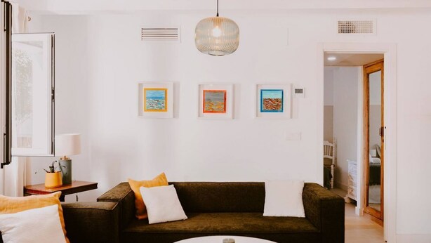 Un soggiorno moderno con un divano marrone scuro, cuscini bianchi, un tavolino da caffè bianco e opere d'arte incorniciate al muro.