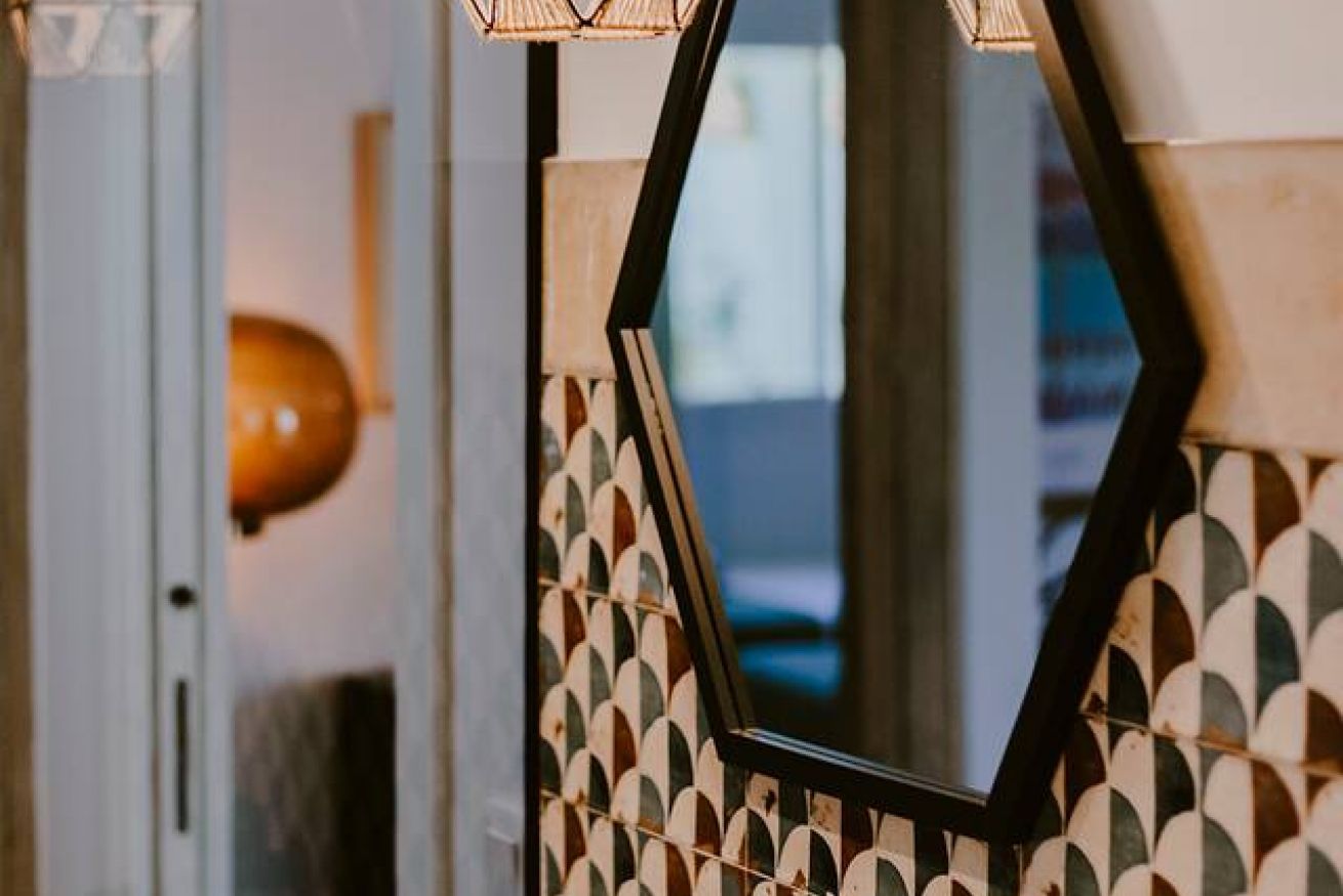 Pared con un diseño geométrico y un espejo hexagonal que refleja una habitación.