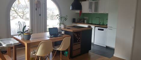 A modern kitchen with white cabinets, a wooden dining table, and a laptop on the table.
