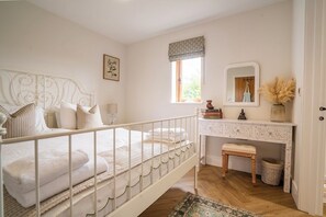 Une chambre à coucher avec un lit en métal blanc, une table de chevet avec un miroir et une fenêtre donnant sur un paysage verdoyant.