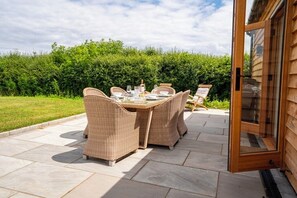 Une terrasse extérieure avec des meubles en osier et une porte vitrée donnant accès à un bâtiment en bois.