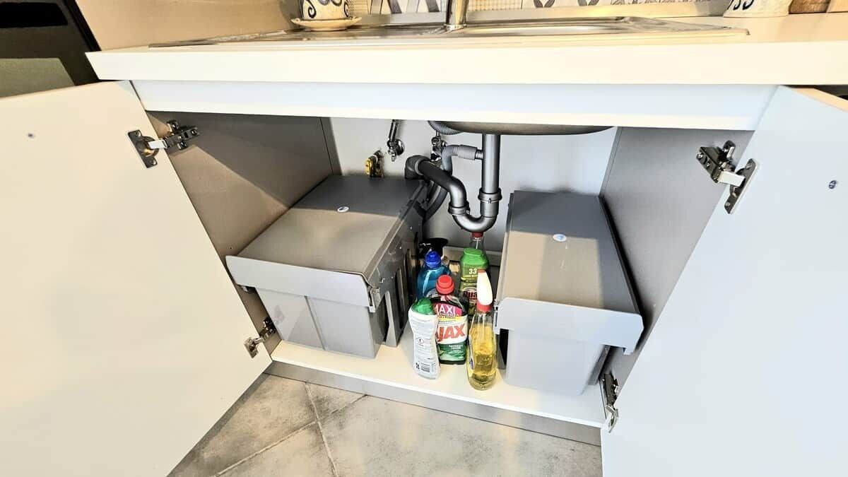 A kitchen with a white countertop, a sink, and various cleaning products.