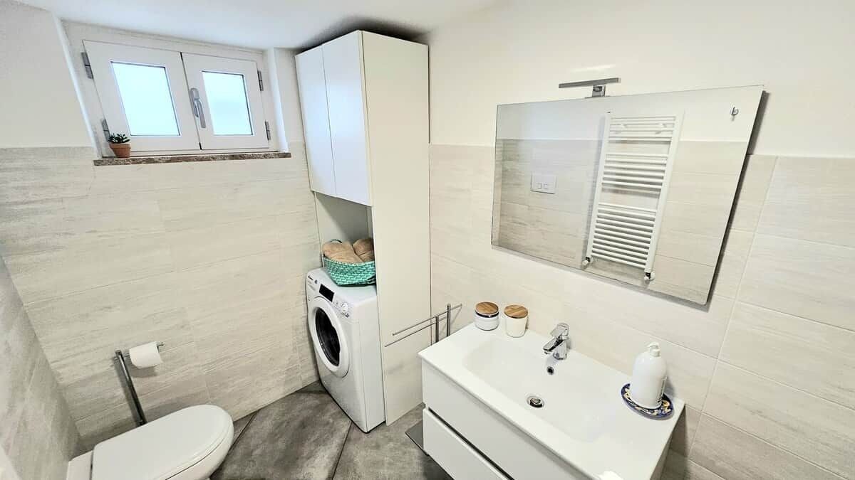 Un bagno compatto con il water, una lavatrice e un lavandino con uno specchio sopra.