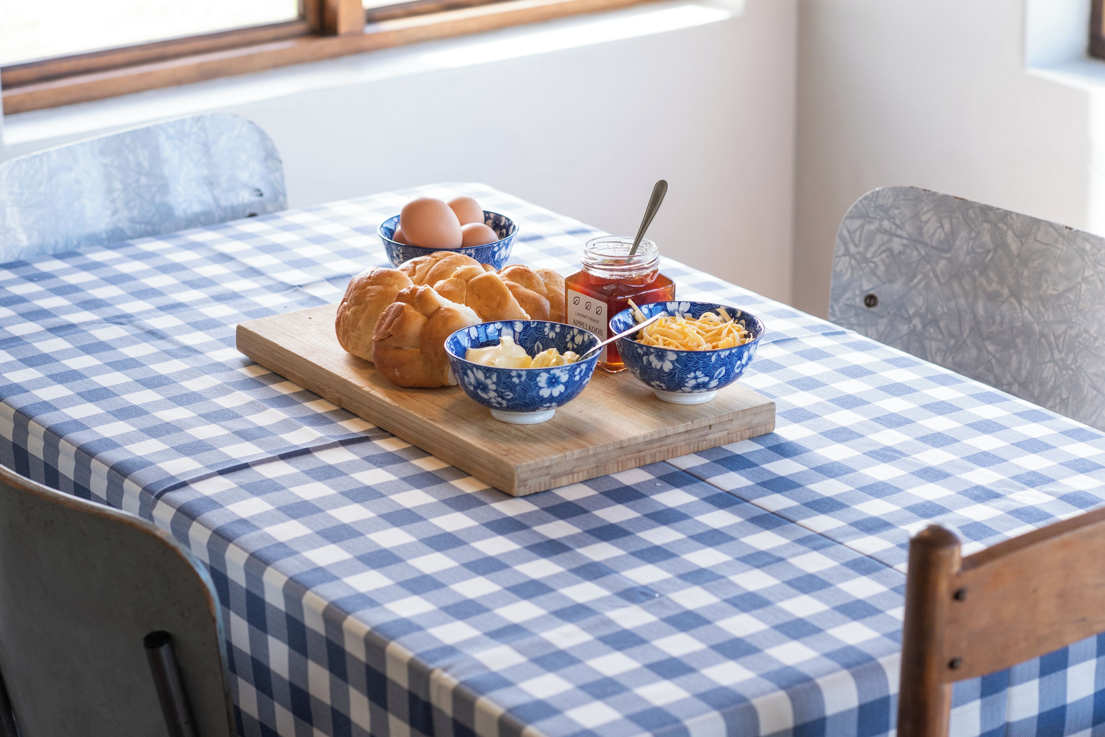 A breakfast setting with bread, eggs, butter, and jam on a checkered tablecloth.