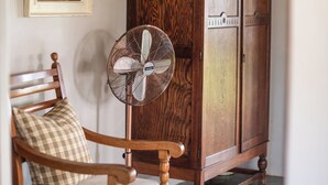 Una silla de madera con cojín, un ventilador de pared y un mueble de madera con una cesta encima.