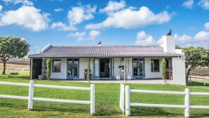 Una casa de una planta con techo plano, un porche delantero y patio cercado.
