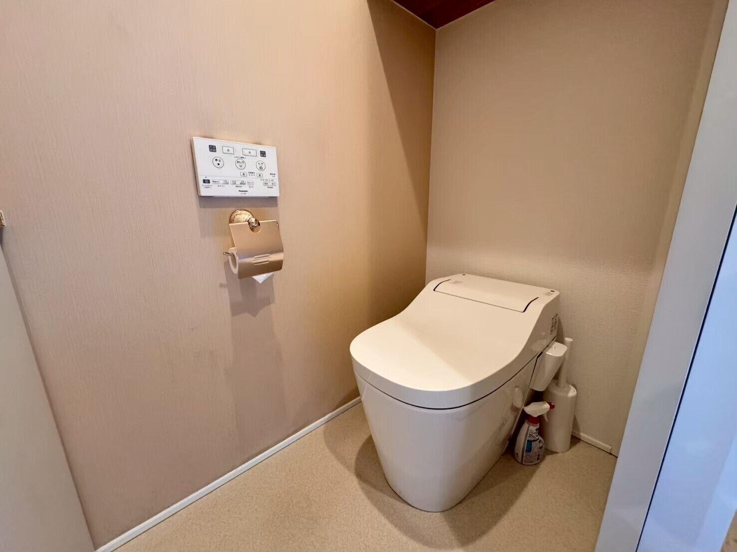 A small, compact bathroom with a toilet, a paper towel dispenser, and a hand sanitizer dispenser.