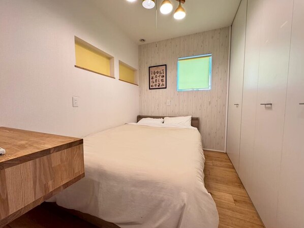 Une chambre à coucher comprenant un lit, une table de chevet, un plancher en bois, une étagère fixée au mur, une fenêtre et un tableau encadré.