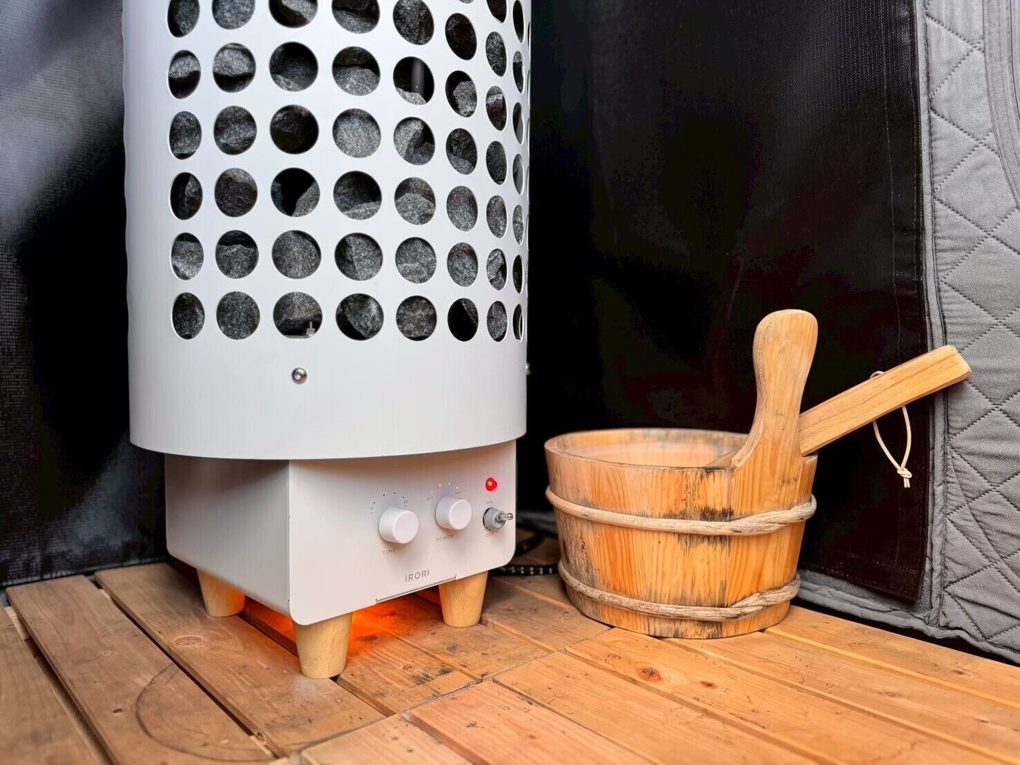 Un appareil de chauffage portatif, doté d’un boîtier blanc et d’ouvertures circulaires, d’un panneau de commande avec des boutons et d’un seau en bois muni d’une poignée.