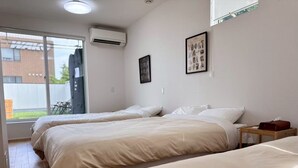 A hotel room with two beds, a window, an air conditioner, and a framed picture on the wall.