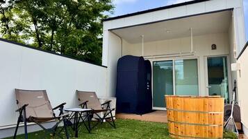 Un patio al aire libre con una mesa y sillas, un barril de madera y una zona cubierta.