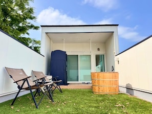 En moderne bygning med fladt tag, en overdækket terrasse med to liggestole og en træfad.