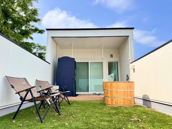 A modern building with a flat roof, a covered patio area with two lounge chairs, and a wooden barrel. - 10 minutes from Okayama Station | Entire property rental | Up to 10 guests | Pets allowed | Tent sauna | 1 parking space | 5 beds | 2 restrooms | Infants and toddlers welcome | (Okayama City)