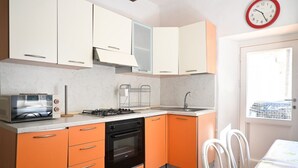 Ett kompakt kök med vita och orange skåp, en gasspis, en ugn och ett fönster med utsikt.