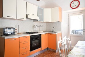 Eine kleine Küche mit weißen und orangefarbenen Schränken, einem Gasherd, einem Backofen und einem Fenster mit Blick.