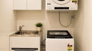 A compact laundry room with a washing machine, a dryer, a sink, and a small plant. - Modern Apartment Near Stadium & Shops (Lidcombe)