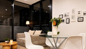 A modern living room with a sofa, white chairs, a glass table, and a vase with flowers. - Modern Apartment Near Stadium & Shops (Lidcombe)