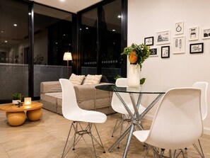 A modern living room with a sofa, white chairs, a glass table, and a vase with flowers. - Modern Apartment Near Stadium & Shops (Lidcombe)