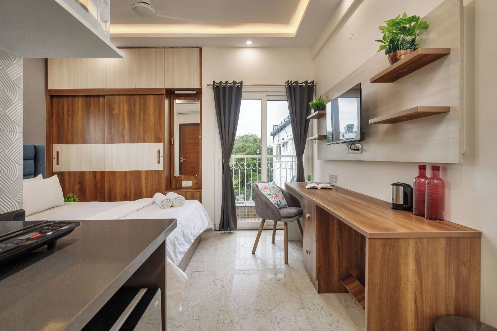 A modern hotel room with a bed, desk, and balcony.