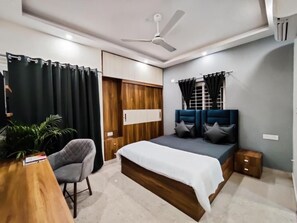 A bedroom with a bed, a desk, a chair, a ceiling fan, and a window with curtains.
