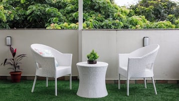 Un espacio al aire libre con dos sillones blancos de mimbre y una pequeña mesa, rodeado de césped artificial y una pared con una maceta.