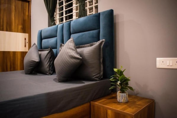 A bedroom with a bed, pillows, a bedside table with a plant, and a wooden wardrobe. - Bluo Studio Koramangala (Bengaluru)