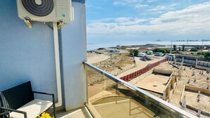 Un balcón con vistas a una obra en construcción, una mesa con un jarrón de girasoles y un equipo de aire acondicionado.