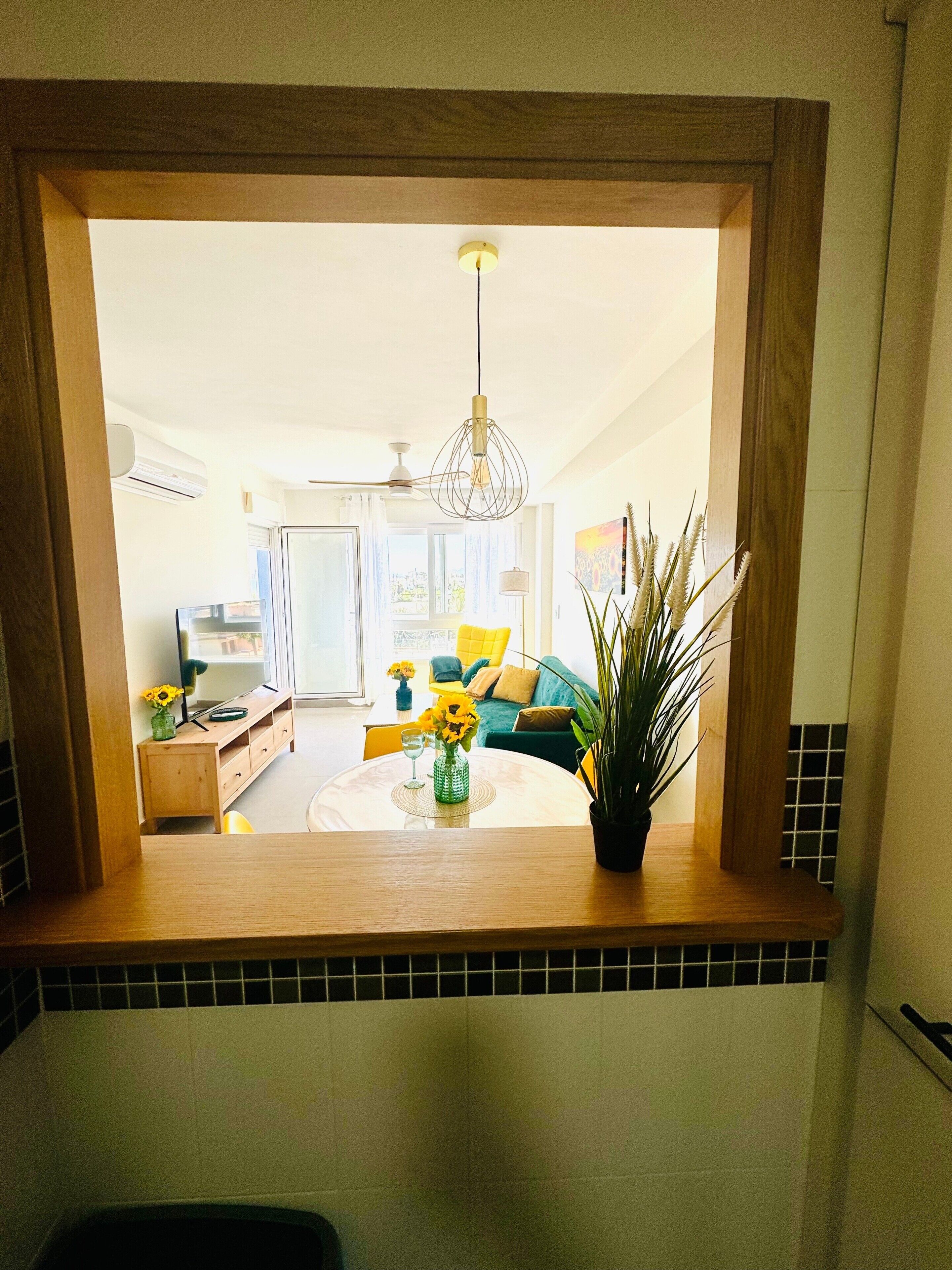 Blick durch ein Fenster in ein Wohnzimmer mit rundem Tisch, Blumentopf und Deckenventilator.