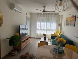 A living room with a TV, sofa, coffee table, and a dining table with chairs.