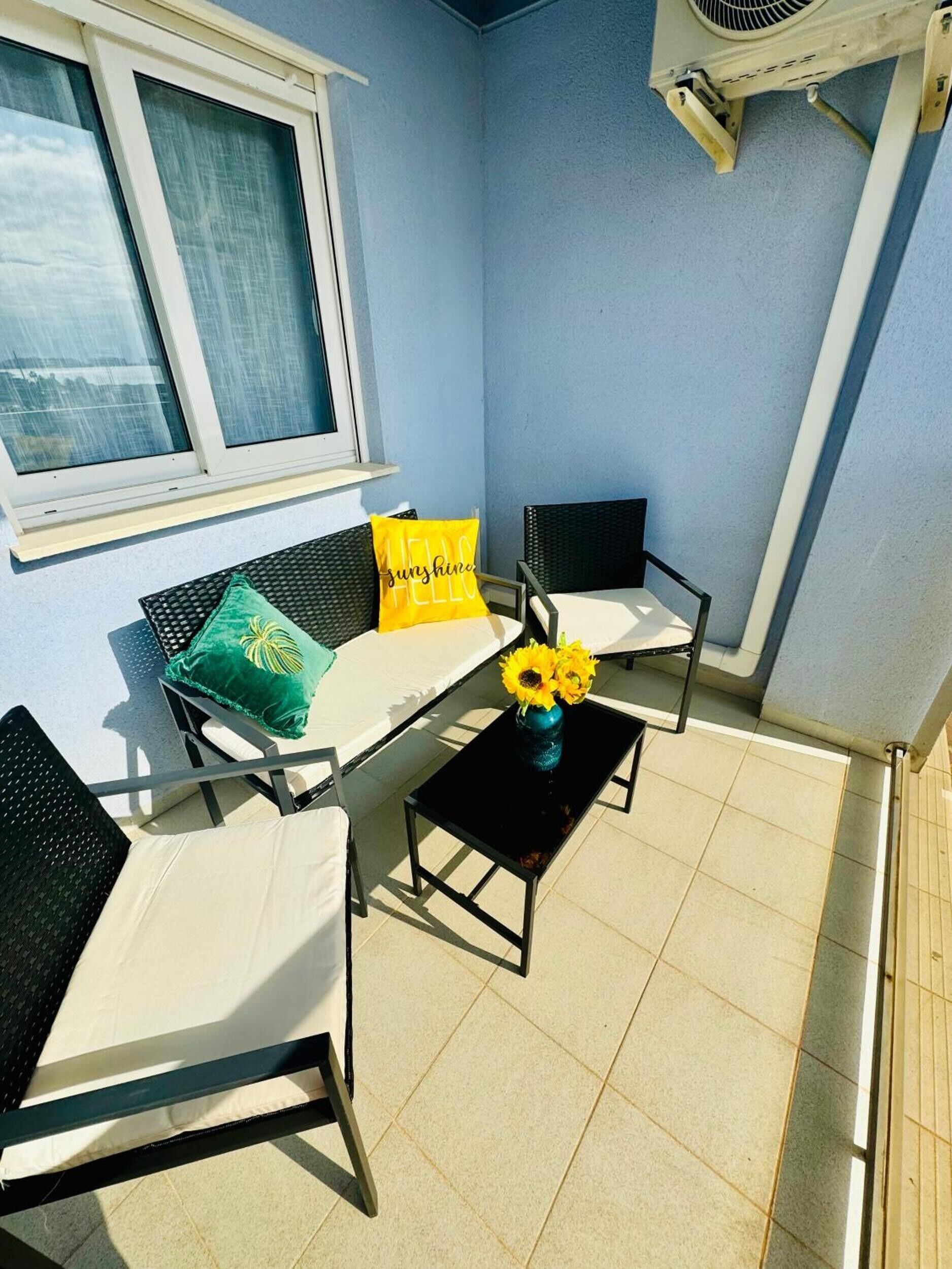 A small balcony with a sofa, two chairs, a table, and a vase with sunflowers.