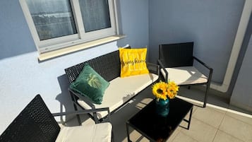 Un balcon avec deux chaises, une petite table et une fenêtre avec des rideaux.