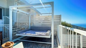 Ein Balkon mit einem Bett, einer Steinmauer und Blick aufs Meer.
