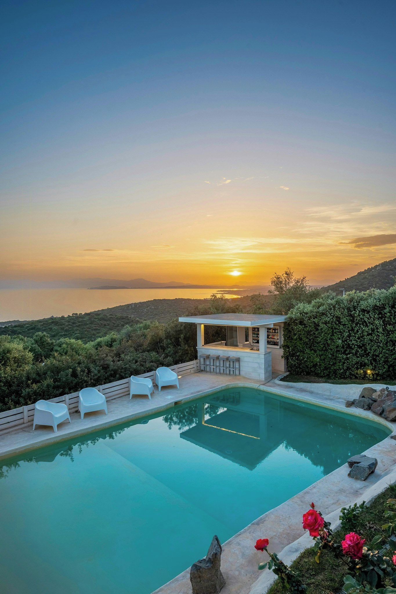 A swimming pool with lounge chairs and a bar area, surrounded by greenery and overlooking a scenic landscape.