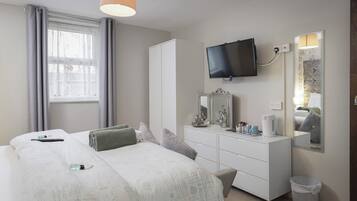 Une chambre d’hôtel avec un lit, une commode, une télévision et une fenêtre avec des rideaux.