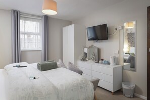 A hotel room with a bed, a dresser, a television, and a window with curtains. - Devon Guest House (Blackpool)